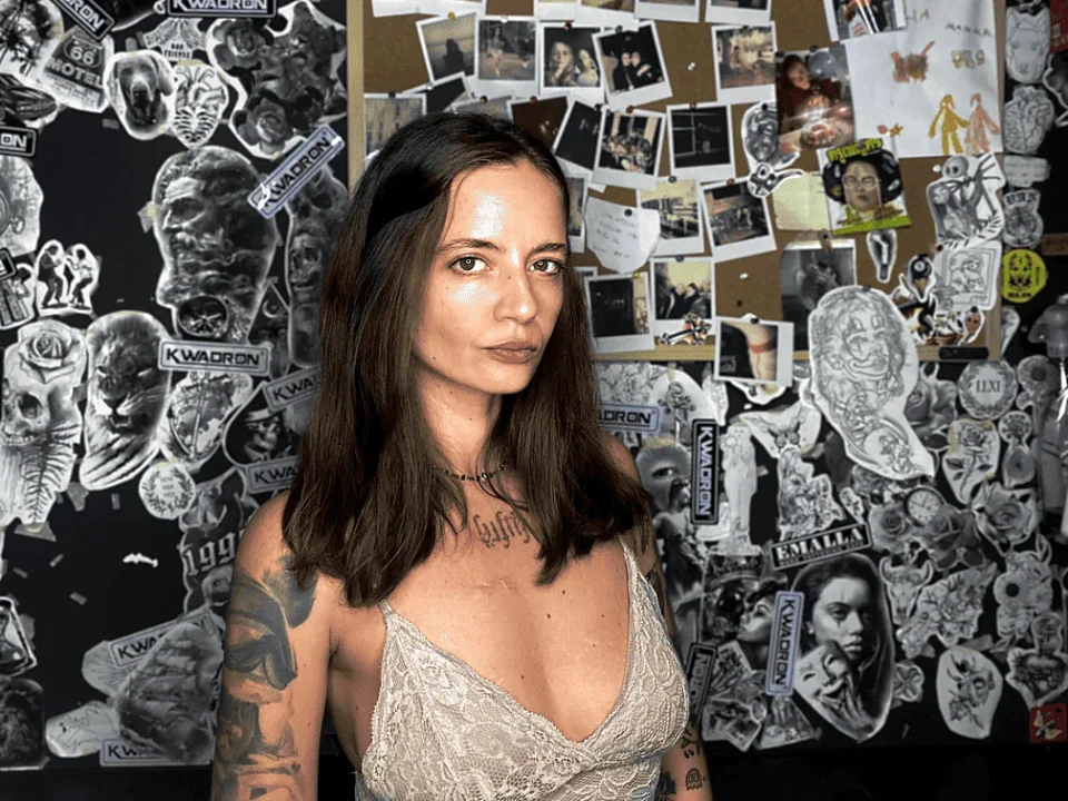 Ritratto di Blerina, tatuatrice dello studio Bunker Tattoo a Monopoli, davanti alla parete di disegni.