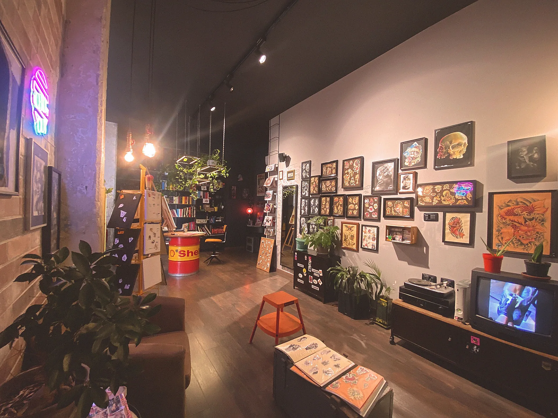 Vista dello studio: insegna al neon, disegni di tatuaggi incorniciati, piante e TV vintage