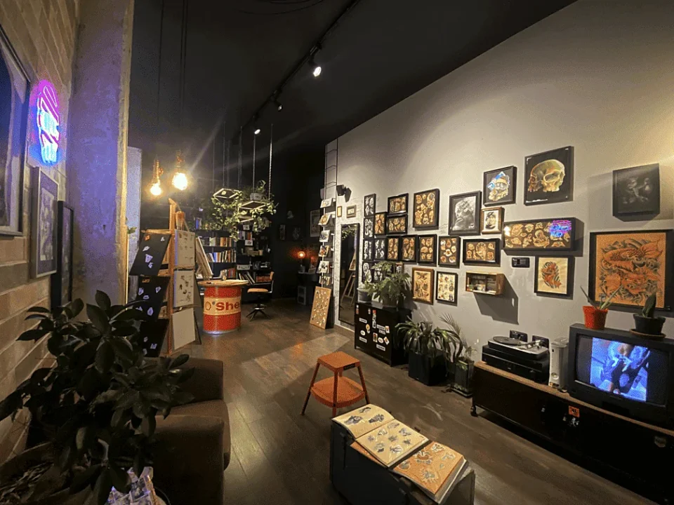 Sala d’attesa di Bunker Tattoo a Monopoli con stampe incorniciate, piante, divano e televisore vintage.