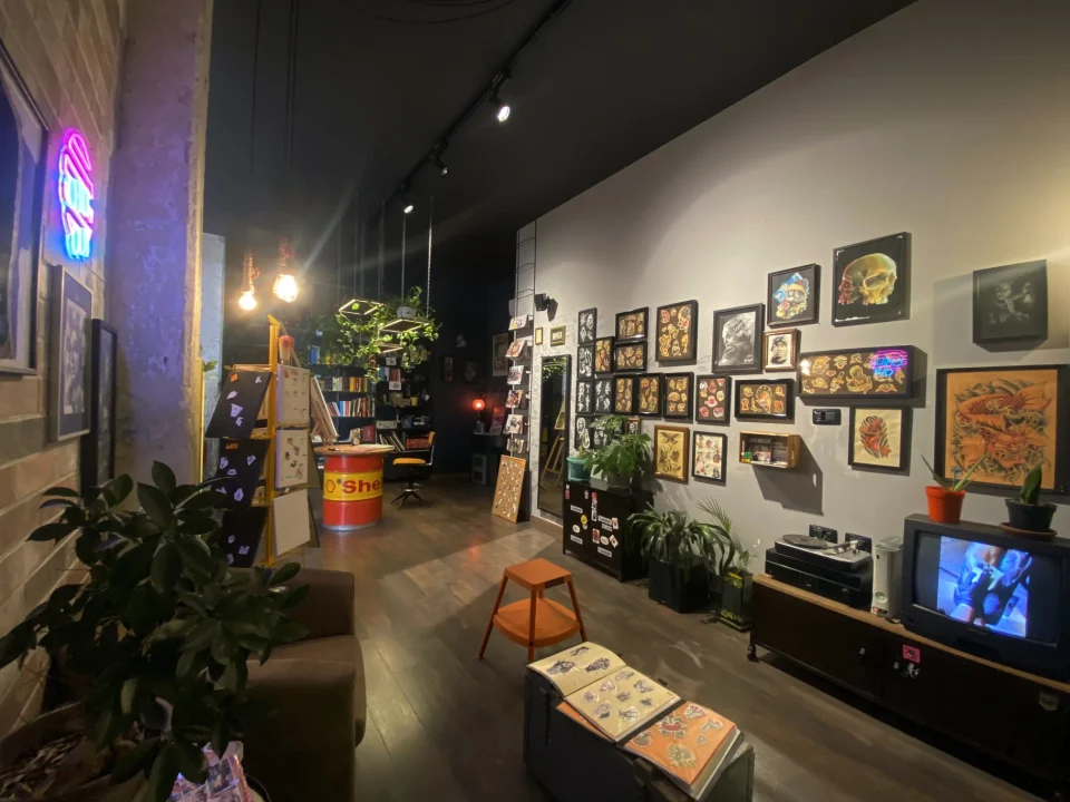 Sala d’attesa di Bunker Tattoo a Monopoli con stampe incorniciate, piante, divano e televisore vintage.